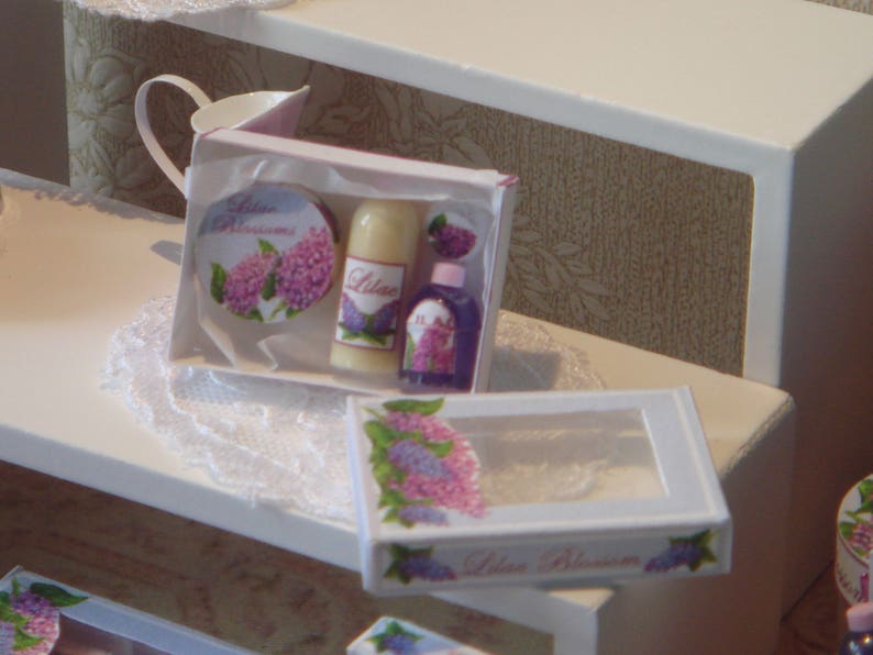 May include: A set of three miniature bath products in a white box with a lilac floral design. The box says "Lilac Blossoms" and contains a bottle of body wash, a bottle of lotion, and a small bottle of bath salts.