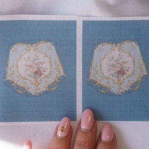 Könnte beinhalten: Zwei blaue Stoffquadrate mit einem goldenen und weißen Blumendesign in der Mitte jedes Quadrats.