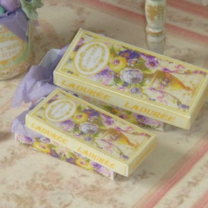 May include: Two yellow boxes with floral designs and the text "Ladurée" on them. The boxes are stacked on top of each other.
