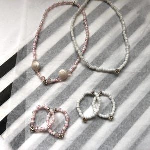 May include: Two pink and white beaded necklaces and two white beaded bracelets. The necklaces have shell accents.