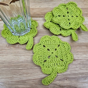 May include: Four green crocheted clover-shaped coasters on a wooden surface.