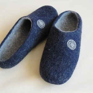 Puede incluir: Un par de zapatillas de lana azul oscuro con forro de fieltro gris. Cada zapatilla tiene un diseño de círculo blanco en la parte superior.