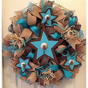 May include: A turquoise and brown star-shaped wreath with burlap and brown ribbon accents. The wreath features three large stars with brown outlines and silver accents.