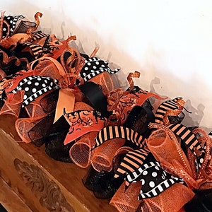 May include: A Halloween-themed door swag with orange, black, and white mesh, ribbon, and polka dot fabric. The swag is decorated with a variety of Halloween-themed embellishments, including a witch's hat, a spider, and a ghost.