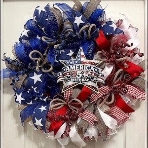 May include: A patriotic wreath with blue, white, and red ribbons and bows. The wreath features a star-shaped emblem with the text "America 250th Birthday". The wreath is a festive decoration for celebrating Independence Day.