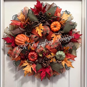 May include: A fall-themed wreath with orange, red, and green accents. The wreath features faux pumpkins, pinecones, and colorful leaves. The text "CK Dazzling Design" is visible on the wreath.