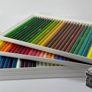 May include: A set of colored pencils arranged in a white tray. The pencils are a variety of colors, including green, yellow, red, and blue. The pencils are neatly organized, suggesting a focus on art supplies and creative tools.