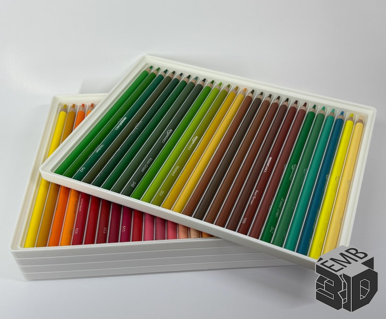 May include: Two white rectangular trays filled with colored pencils. The pencils are arranged in rows by color, ranging from yellow to red, green, and brown. The pencils are neatly organized, creating a visually appealing display.