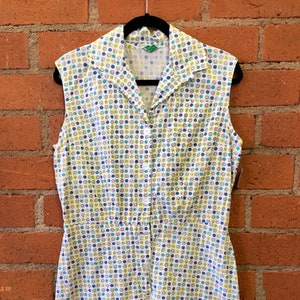 May include: A white sleeveless button-up dress with a green collar and a pattern of blue, green, and brown circles.