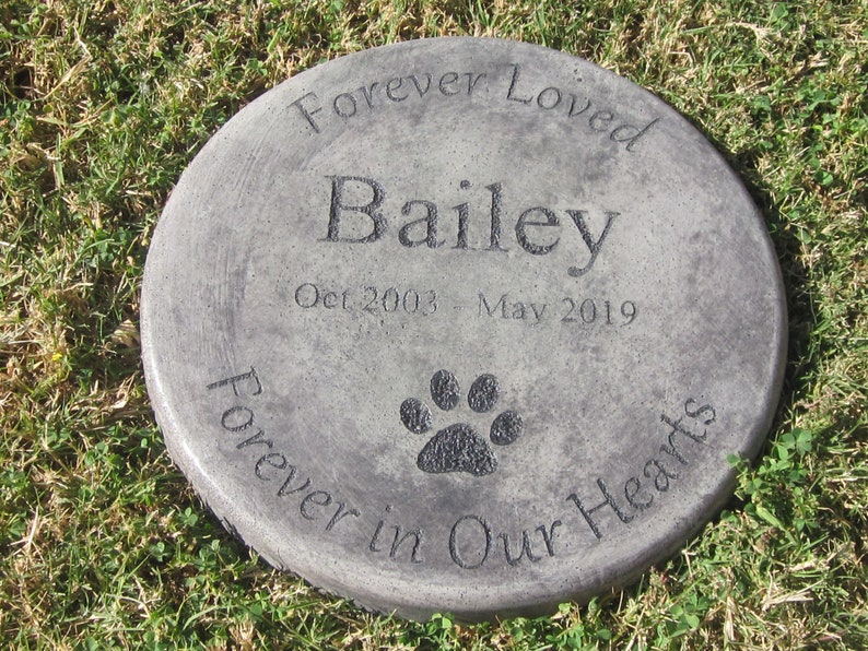 以下が含まれることがあります： 「Forever Loved Bailey Oct 2003 - May 2019 Forever in Our Hearts」と肉球の跡が刻まれた灰色のコンクリート製の記念碑