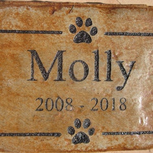 May include: A brown rectangular stone memorial with black engraved text. The text reads "Molly 2008 - 2018" with a paw print above and below the name.