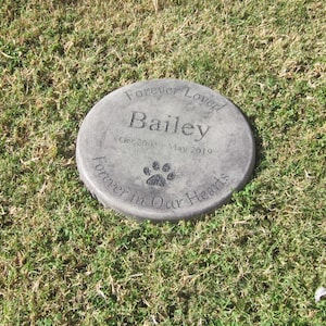以下が含まれることがあります： 「Forever Loved Bailey Oct 2003 - May 2019 Forever in Our Hearts」と肉球の跡が刻まれた灰色のコンクリート製の記念碑