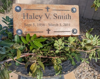May include: A brown rectangular plaque with a cross at the top and bottom. The plaque has the text "Haley V. Smith" and "Sept 5, 1956 - March 3, 2011" engraved on it. The plaque is attached to a planter with screws.