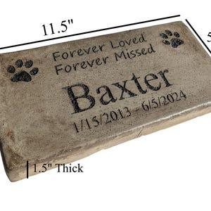 May include: A rectangular, light brown, concrete pet memorial stone with rounded edges. It features the text "Forever Loved Forever Missed" and the name "Baxter" with paw prints and the dates "1/15/2013 - 6/5/2024". The stone measures 11.5 inches long, 5.5 inches wide, and 1.5 inches thick.