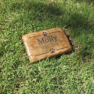 May include: A brown rectangular stone memorial with the name "Molly" and the dates "2008 - 2018" engraved on it.  The stone is surrounded by green grass.