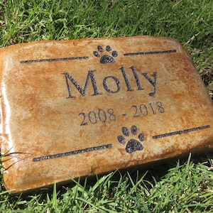 May include: A brown stone pet memorial with black paw prints and the inscription "Molly 2008 - 2018".