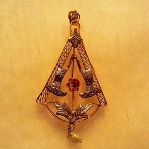 May include: A gold pendant with a delicate filigree design featuring two birds facing each other. The pendant has a red gemstone in the centre and a pearl drop at the bottom.