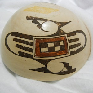 May include: A white ceramic bowl with a brown and black geometric design. The design features a central square with a checkerboard pattern and two curved shapes on either side.