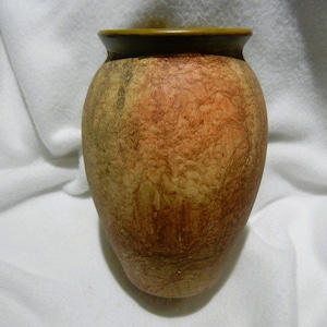 May include: A small, round, brown ceramic vase with a textured surface and a dark brown rim.
