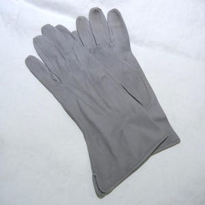May include: A pair of solid light gray gloves featuring a smooth, matte finish. The gloves have stitched detailing along the back of the hand and fingers, with a small notched opening at the wrist hem for a tailored fit and clean appearance.