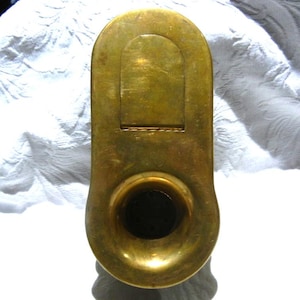 May include: A vintage brass object with a rounded top and a flared bottom. The brass has a warm, golden hue and shows signs of age. The object has a rectangular indentation near the top and a circular opening at the bottom.
