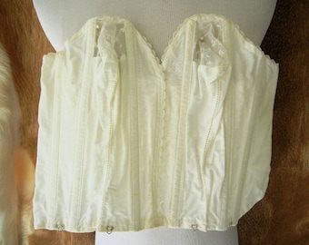 May include: A white cotton corset with lace trim and metal hooks. The corset is a vintage style and has a boned structure.