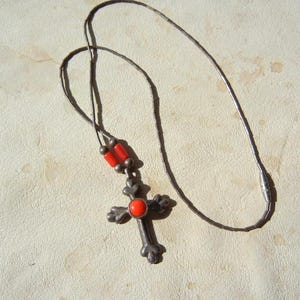 May include: A silver-tone cross pendant necklace with a red gemstone center and red bead accents. The cross has decorative floral-like details. The necklace is on a thin, dark chain.