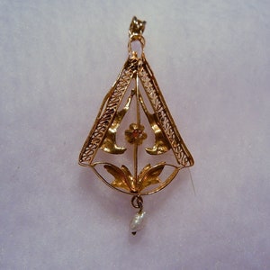 May include: A gold pendant with a delicate filigree design featuring a flower with a red centre and a pearl drop.