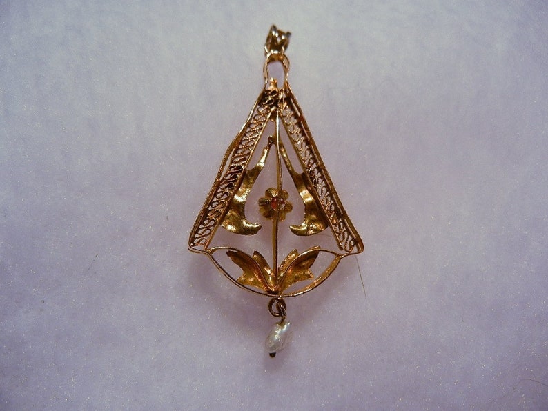 May include: A gold pendant with a delicate filigree design featuring a flower with a red centre and a pearl drop.