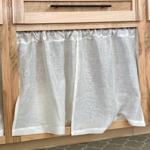 May include: White linen curtains with a gathered top, hanging in front of a wooden cabinet.