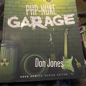 May include: A book cover with a green brick wall background and the text "PHP-NUKE GARAGE" in white. The book title is "PHP-NUKE GARAGE" and the author is "Don Jones". The book cover also features a green trash can with a radiation symbol, a guitar, and a tire.