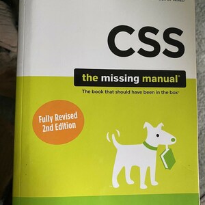 May include: A yellow and green book cover with the title "CSS the missing manual" in black text. The book is a second edition and is fully revised. The cover also features a white dog carrying a green book.