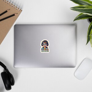 May include: A sticker featuring a cartoon girl wearing headphones and glasses with the text "Just a girl who loves coding".