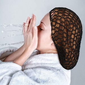May include: A woman with wet hair is wearing a black hair net. She is holding her hands up to her face as water splashes around her.