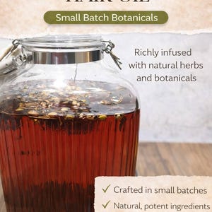 May include: A glass jar filled with herbal-infused hair oil. The oil is a deep reddish-brown color and contains visible herbs and botanicals. Text on the image reads "Herbal-Infused Hair Oil" and "Small Batch Botanicals."
