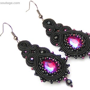May include: A pair of black earrings with a pink gemstone in the center of each earring. The earrings are made of black thread and beads.