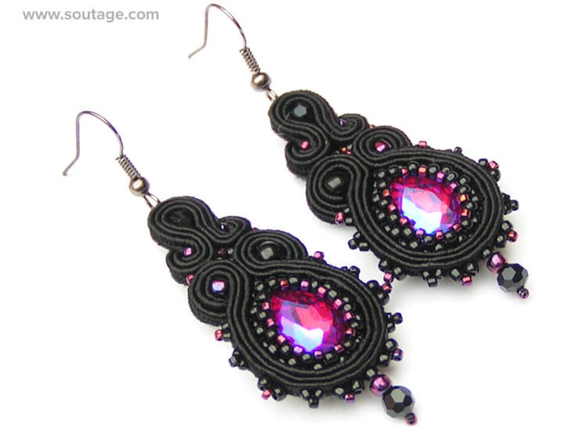 May include: A pair of black earrings with a pink gemstone in the center of each earring. The earrings are made of black thread and beads.