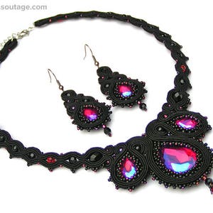 May include: A black and red beaded necklace and earrings set with a teardrop-shaped pendant. The necklace is made of black thread and features a large red crystal in the center.