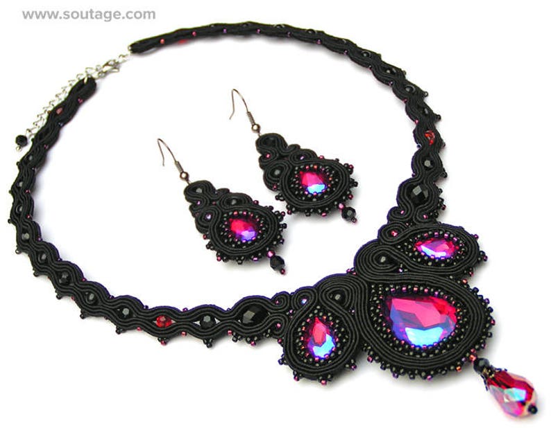 May include: A black and red beaded necklace and earrings set with a teardrop-shaped pendant. The necklace is made of black thread and features a large red crystal in the center.