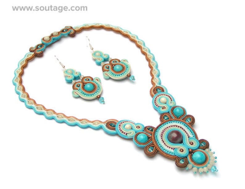 Puede incluir: Un collar y pendientes a juego de cuentas turquesa, marr&oacute;n y blanco. El collar presenta un gran colgante intrincado con una cuenta central marr&oacute;n.