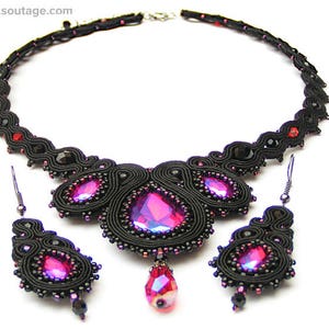 May include: A black and pink beaded necklace and earrings set. The necklace features a large, teardrop-shaped pendant with a pink crystal. The earrings are small and dangle.