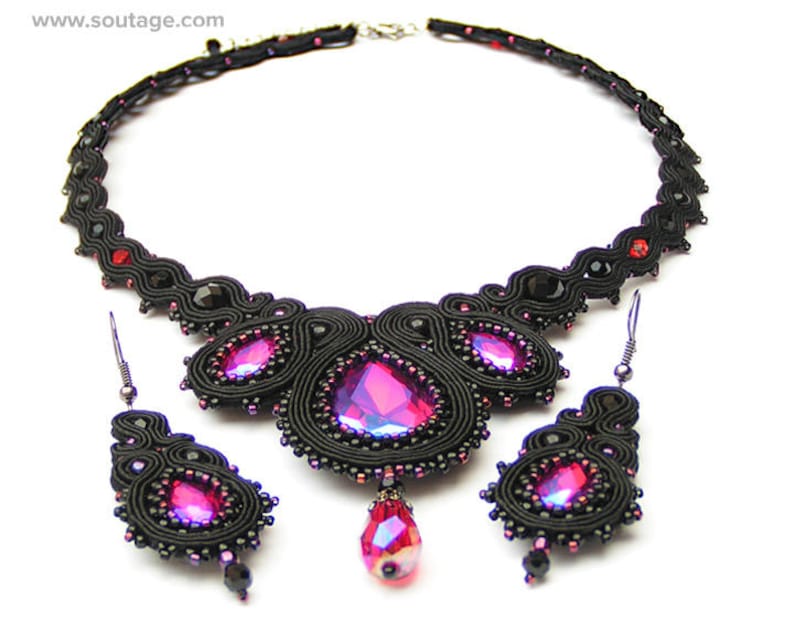 May include: A black and pink beaded necklace and earrings set. The necklace features a large, teardrop-shaped pendant with a pink crystal. The earrings are small and dangle.