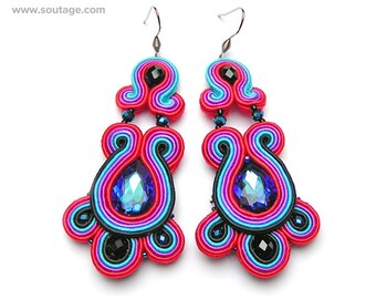 May include: A pair of vibrant, handmade soutache earrings. The earrings feature a teardrop-shaped blue crystal, surrounded by red, pink, blue, and black soutache cord. Small black beads and silver-tone hooks complete the design. The earrings have a unique, artistic style.