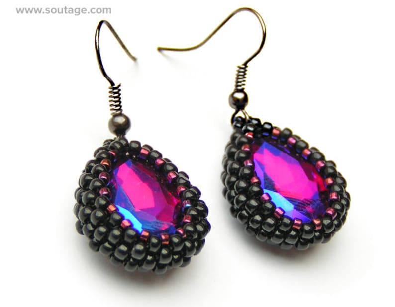 May include: A pair of dangle earrings with black beads and a teardrop-shaped iridescent pink crystal.