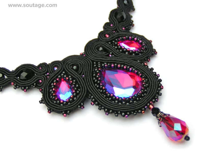 May include: A black beaded necklace with a large, iridescent pink gemstone pendant. The necklace is made of black thread and features a delicate, intricate design.