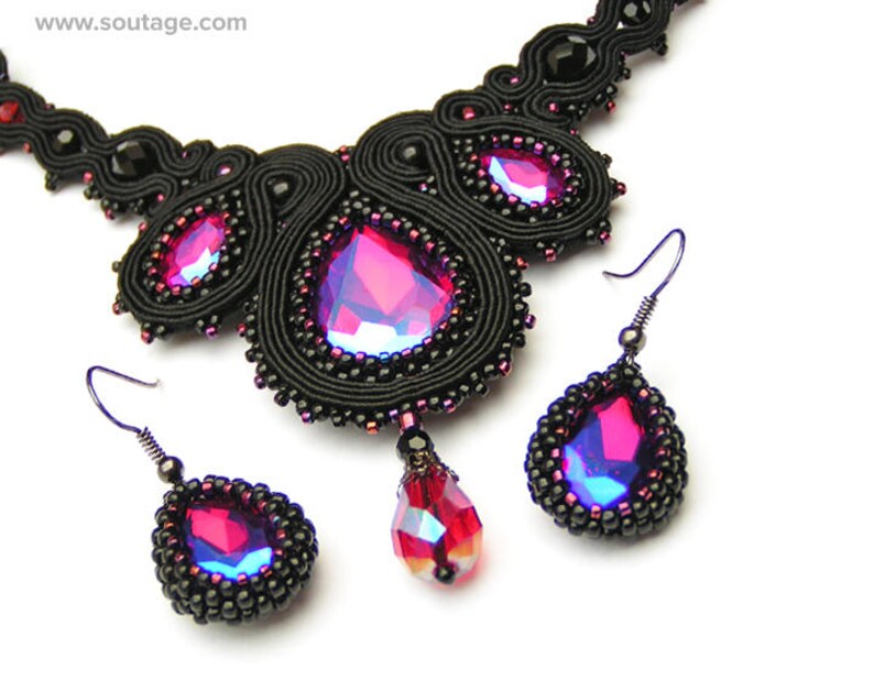 May include: A black beaded necklace and matching earrings with a large, iridescent pink gemstone pendant. The necklace is made of black thread and beads, and the earrings are teardrop shaped.