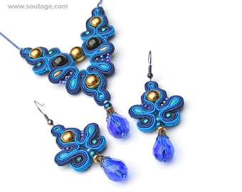 May include: A blue and gold necklace and matching earrings with blue and gold accents. The necklace and earrings feature a unique, intricate design with a teardrop-shaped pendant.
