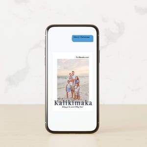 May include: A smartphone displays a family photo on a beach, with the text "Mele Kalikimaka" and "Wishing you the warmest Holiday Season!" in dark blue. A blue text bubble at the top reads "Merry Christmas".