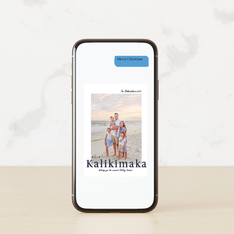 May include: A smartphone displays a family photo on a beach, with the text "Mele Kalikimaka" and "Wishing you the warmest Holiday Season!" in dark blue. A blue text bubble at the top reads "Merry Christmas".
