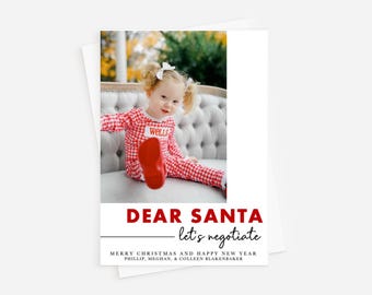 May include: Christmas card featuring a young child in red and white checkered pajamas, seated on a tufted gray sofa. The card reads "DEAR SANTA let's negotiate" in red text. The child's name "Wells" is visible on the pajamas.